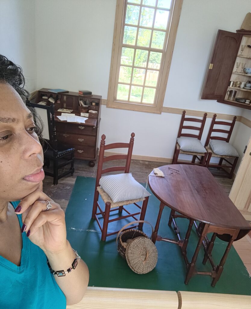 A woman stands in profile, pondering a room wooden, colonial-style desks and chairs. 